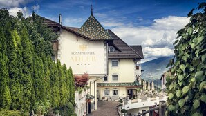 A hotel with a prominent sign, a cobblestone path leading to the entrance, and a mountainous backdrop. - Sonnenhotel Adler (Villandro)