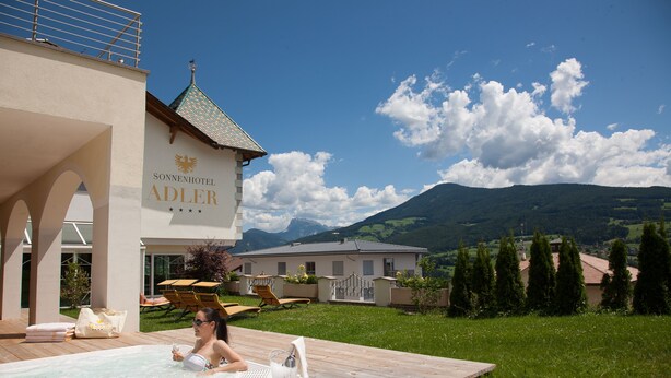 A hotel with a swimming pool, outdoor seating, and a view of mountains. - Sonnenhotel Adler (Villandro)