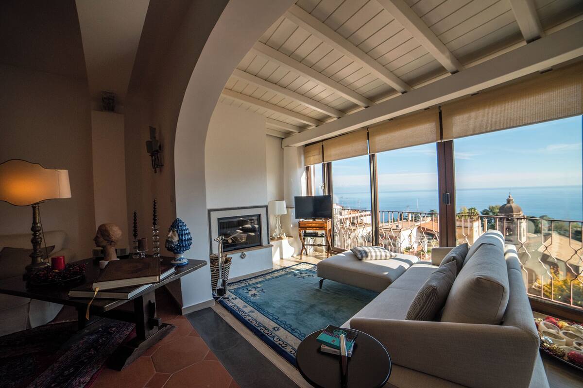 Ein geräumiges Wohnzimmer mit großem Fenster und Ausblick auf eine schöne Landschaft, einem Kamin und bequemen Sitzmöglichkeiten.
