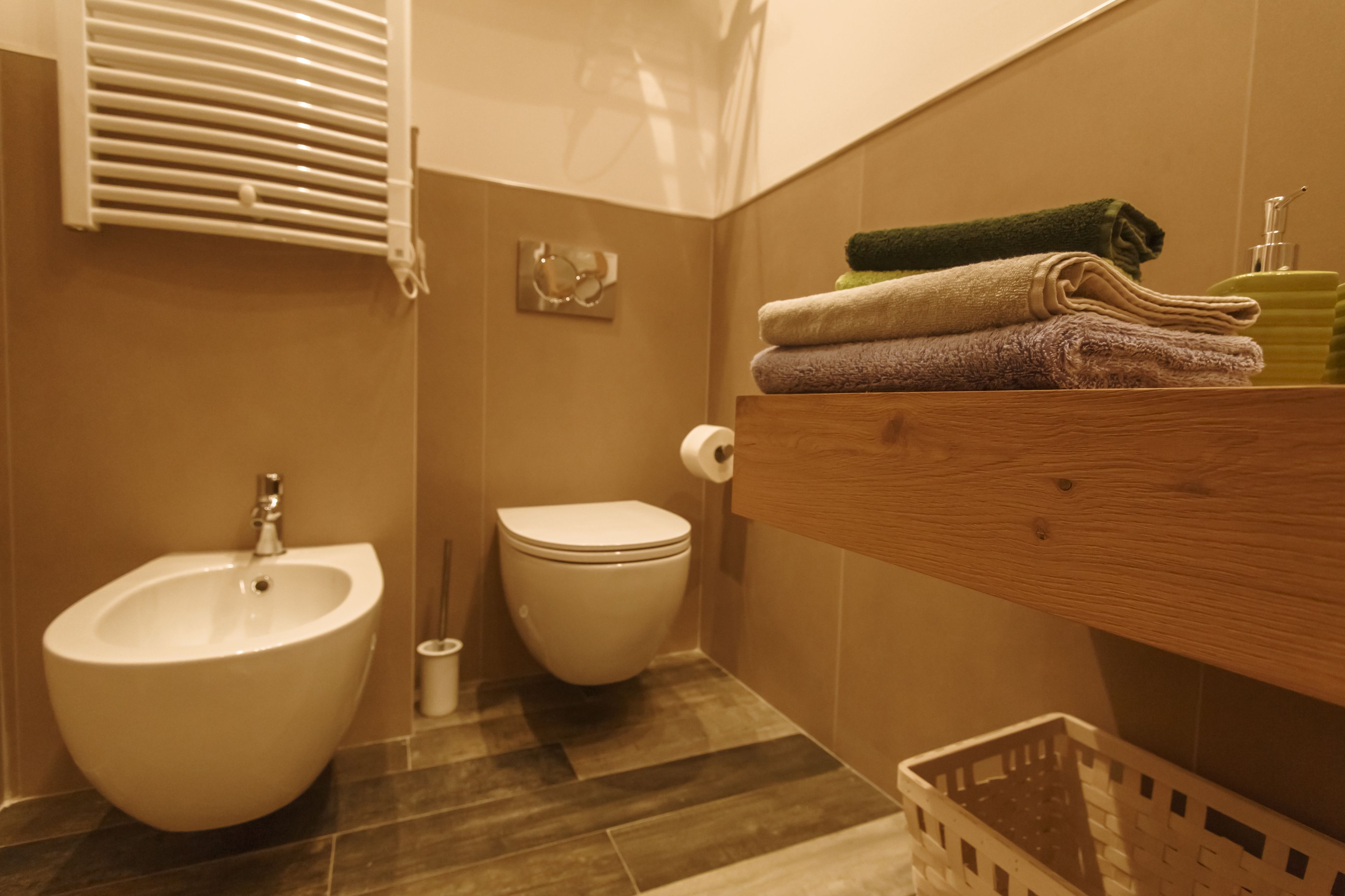 Un baño con bidé, inodoro y un estante de madera con toallas.