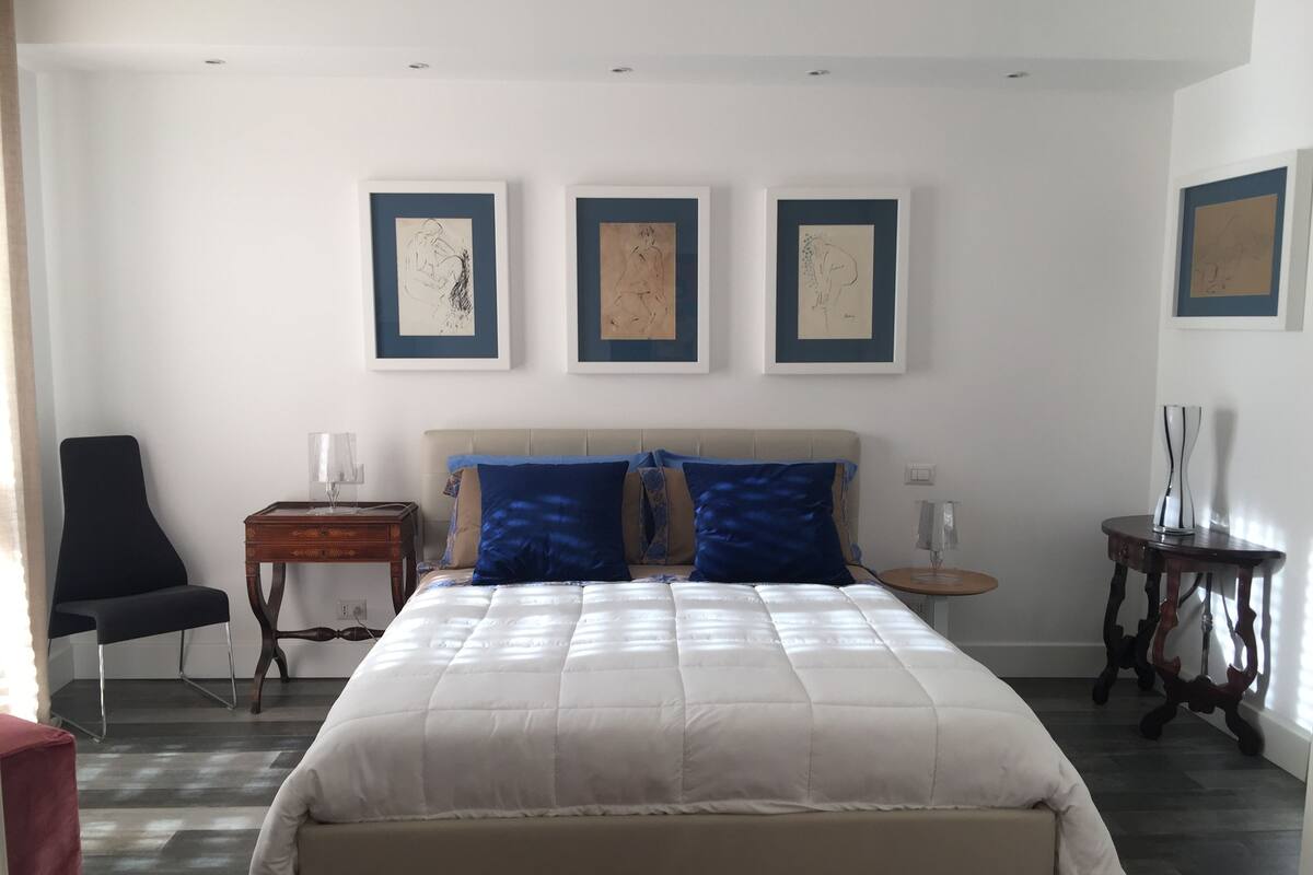 Ein Schlafzimmer mit einem großen Bett, einem Sessel, einem kleinen Tisch und drei gerahmten Kunstwerken an der Wand.
