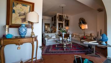 Amplia sala de estar con sofá, mesa de centro y objetos decorativos. Se observa un comedor en el fondo.