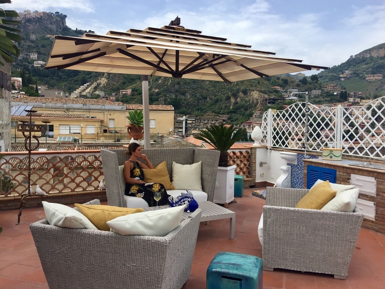 Varanda com móveis de vime, uma mesa e um guarda-sol.