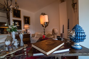 A well-furnished living room with a large book, decorative vases, a bust, and a blue ceramic piece on a wooden table. - Casa Aricò & Shatulle Suites (Taormina)