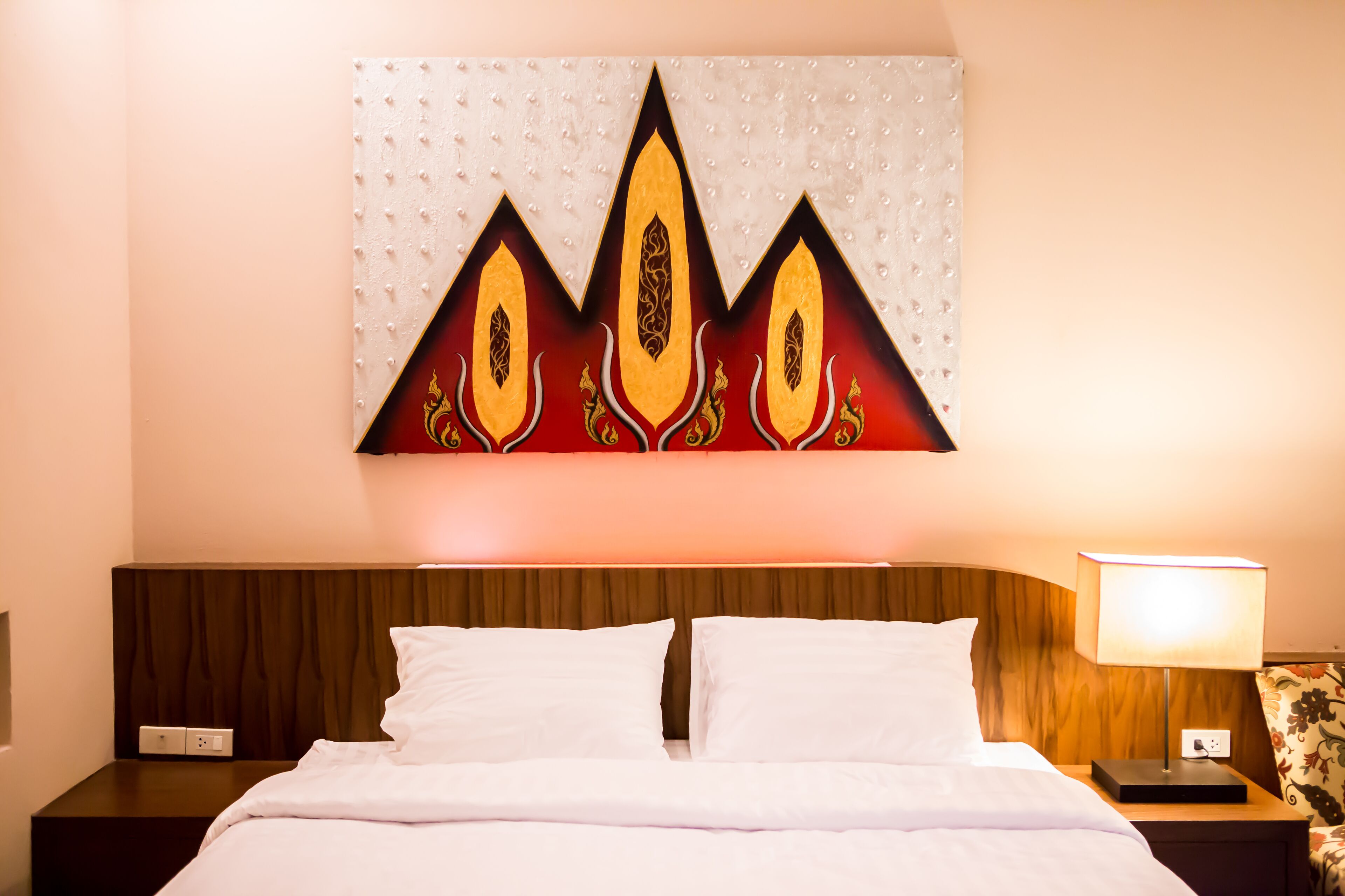 A hotel room with a bed, a nightstand with a lamp, and a wall-mounted artwork.