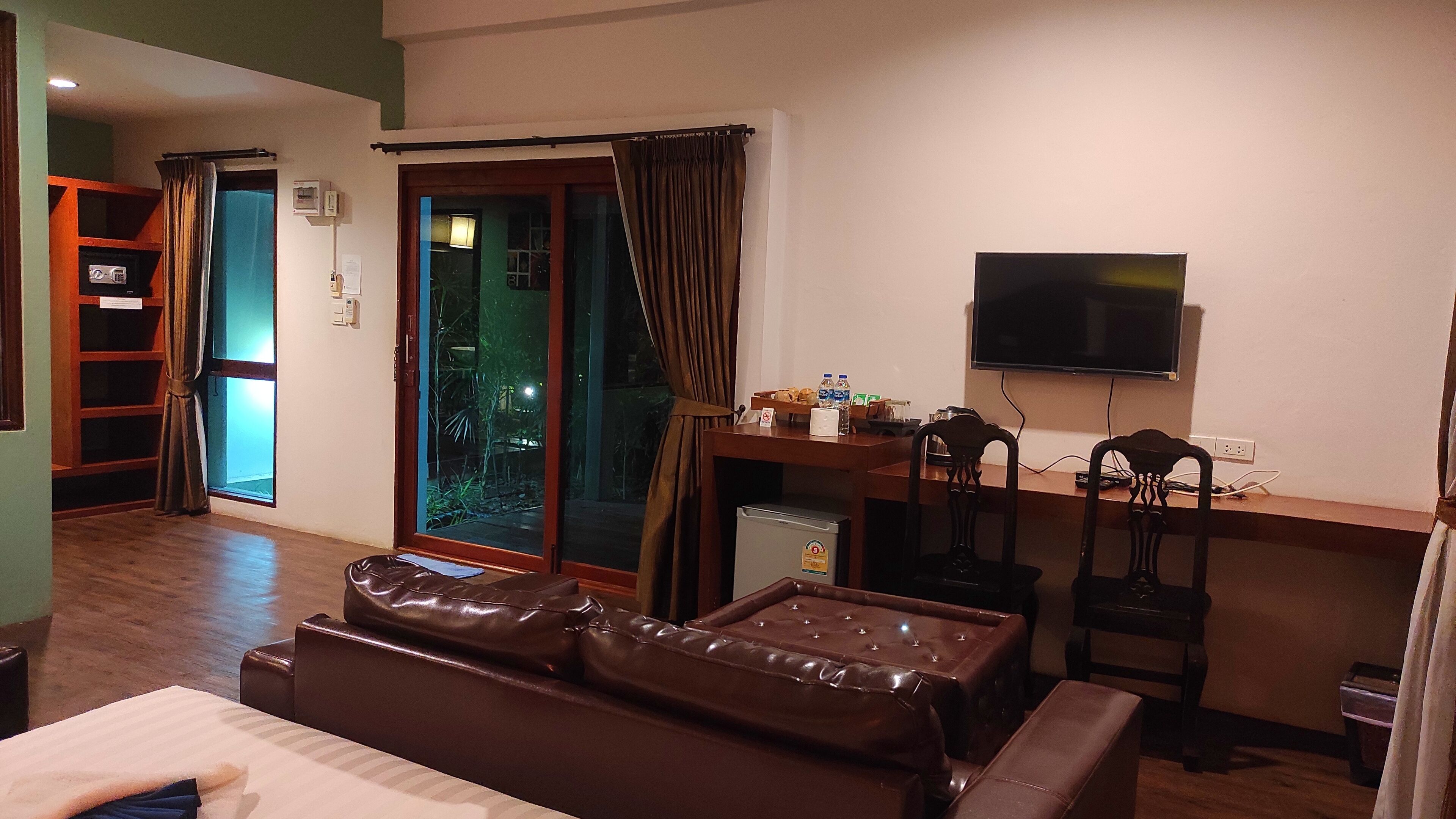 A hotel room with a sofa, a small table with a TV, a refrigerator, and a sliding glass door leading to a balcony.
