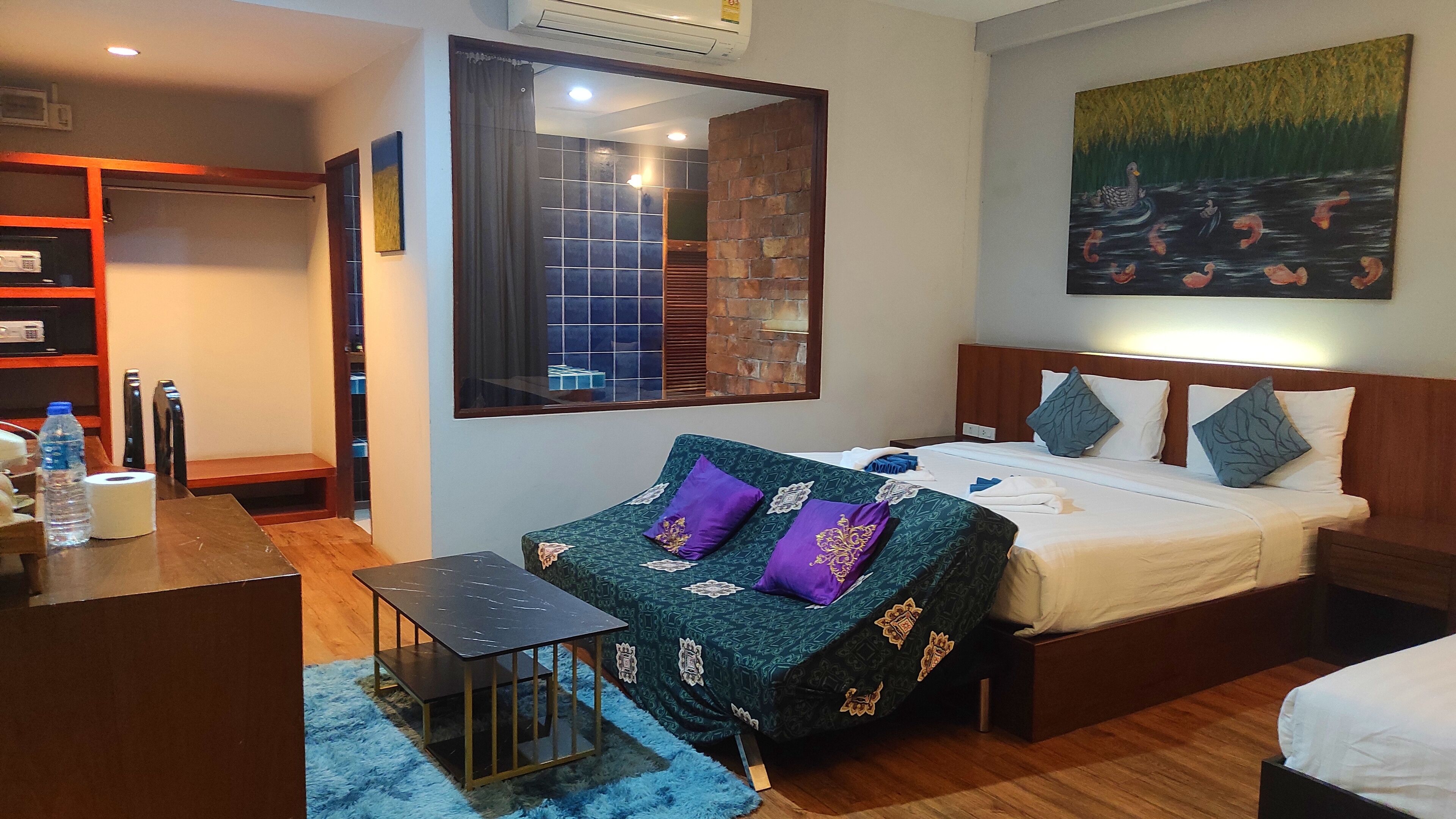 A hotel room with a bed, a sofa, a small table, a mirror, and a painting on the wall.