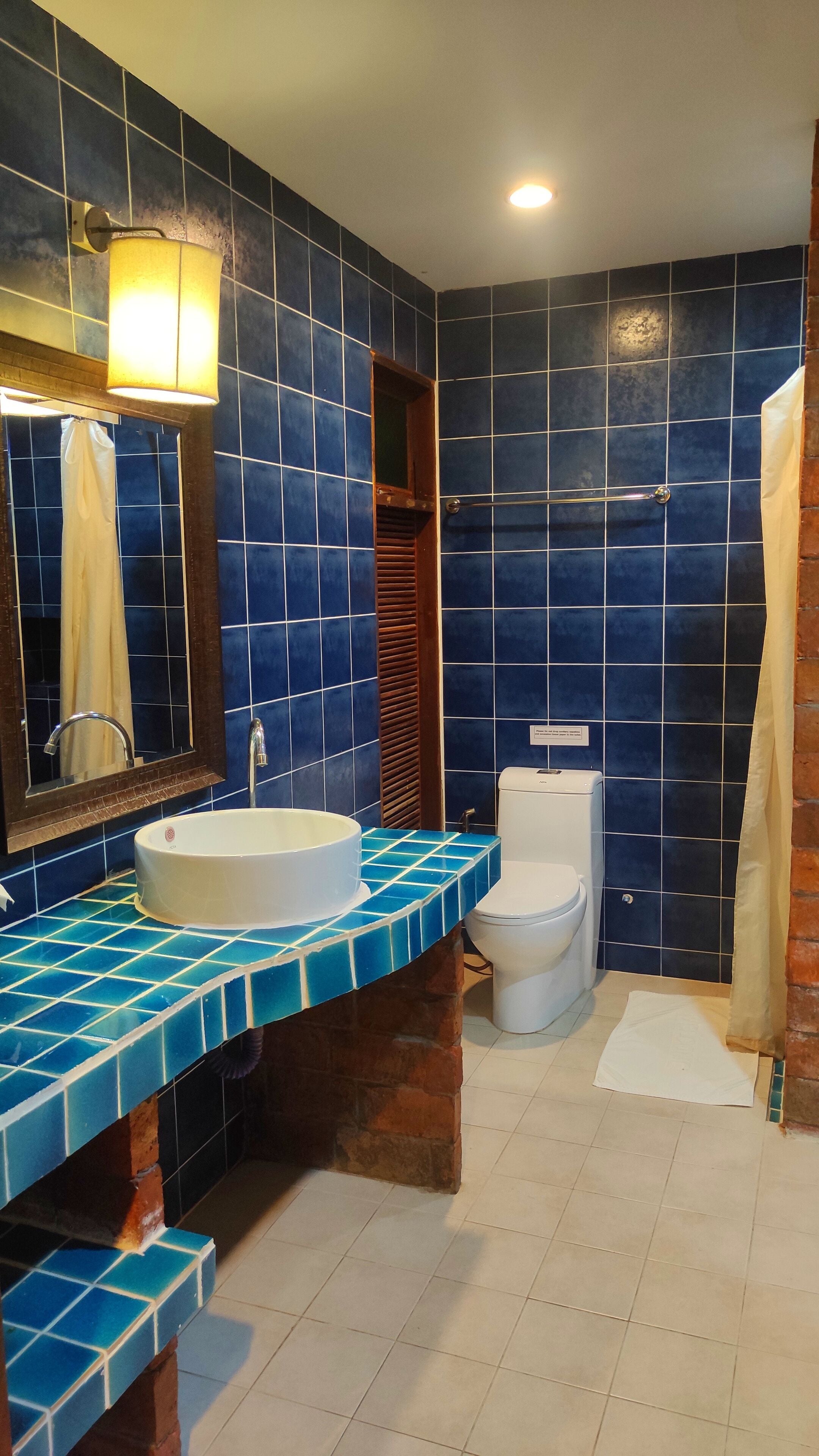 A bathroom with a blue-tiled wall, a white sink, a toilet, and a shower curtain.