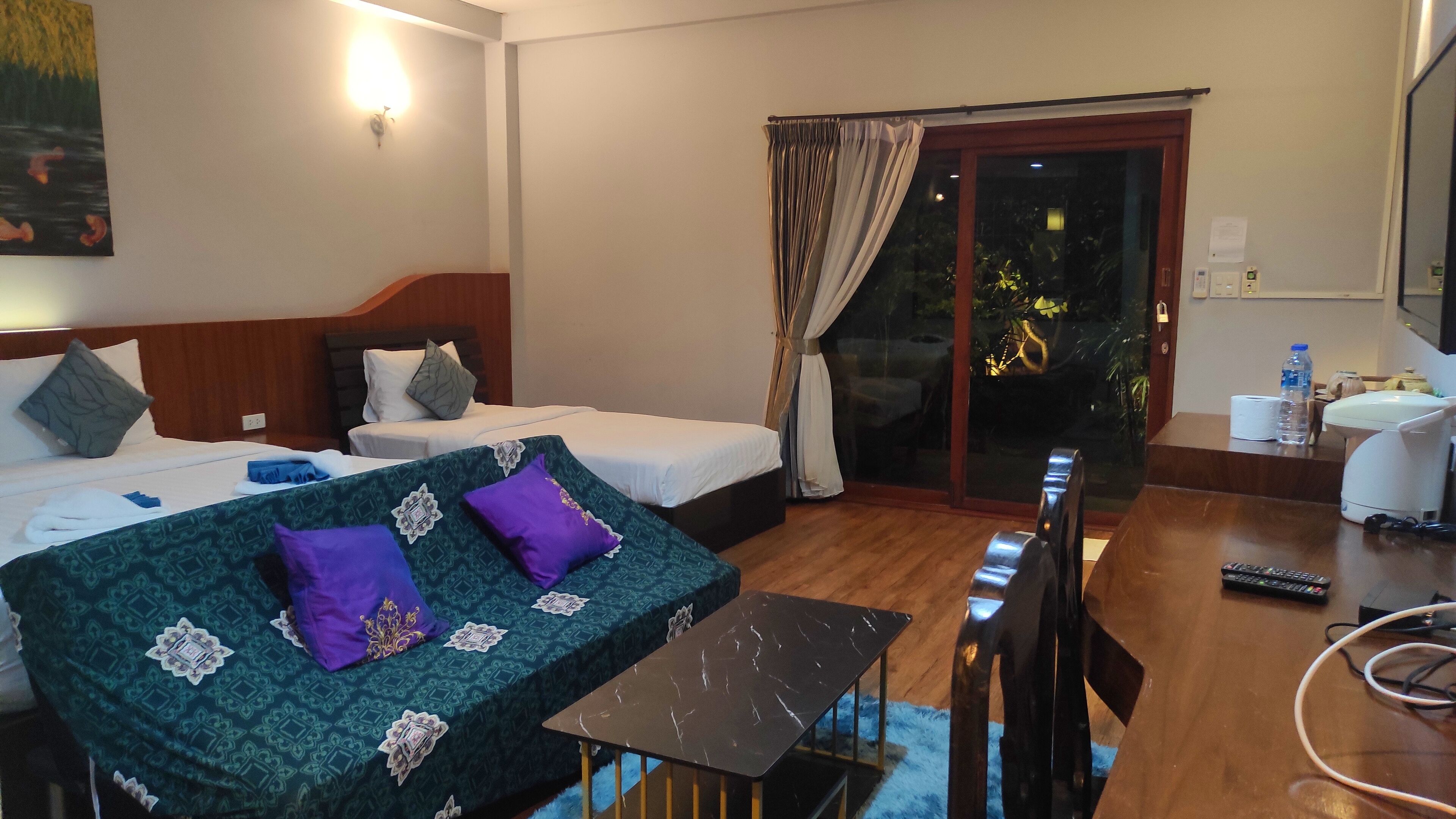 A hotel room with two beds, a sofa, a small table, a TV, and a sliding glass door to the outside.