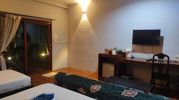 A hotel room with a bed, a desk with a chair, a television, and a sliding glass door leading to an outdoor area.