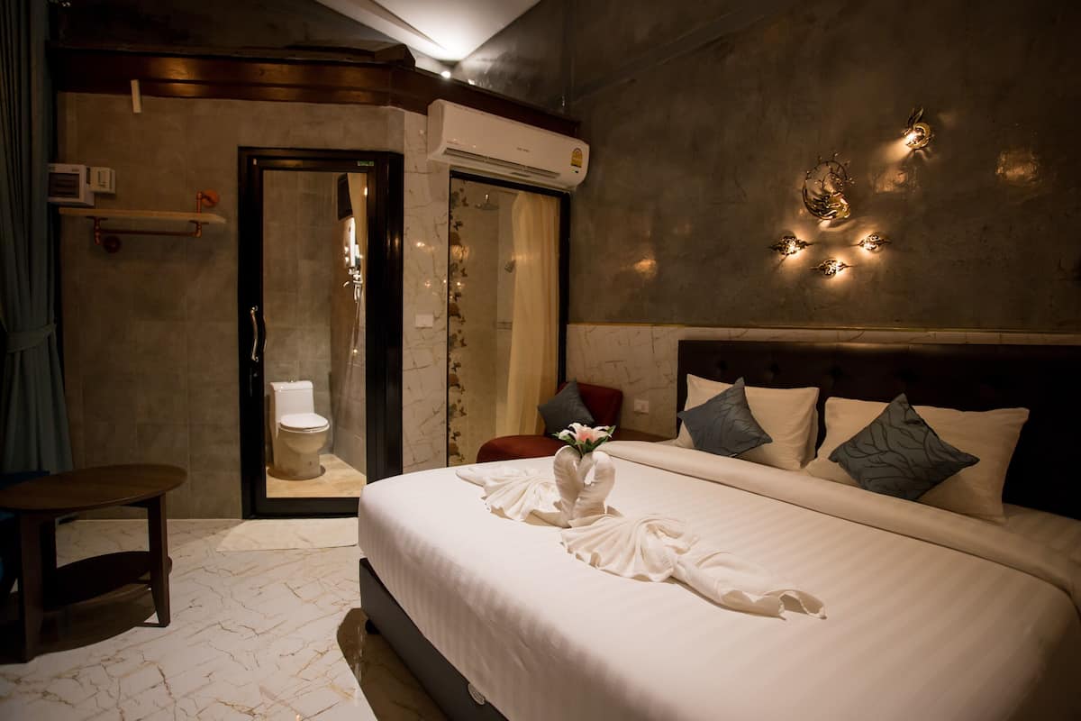 A hotel room with a large bed, a bedside table, a bathroom with a toilet, and an air conditioning unit.