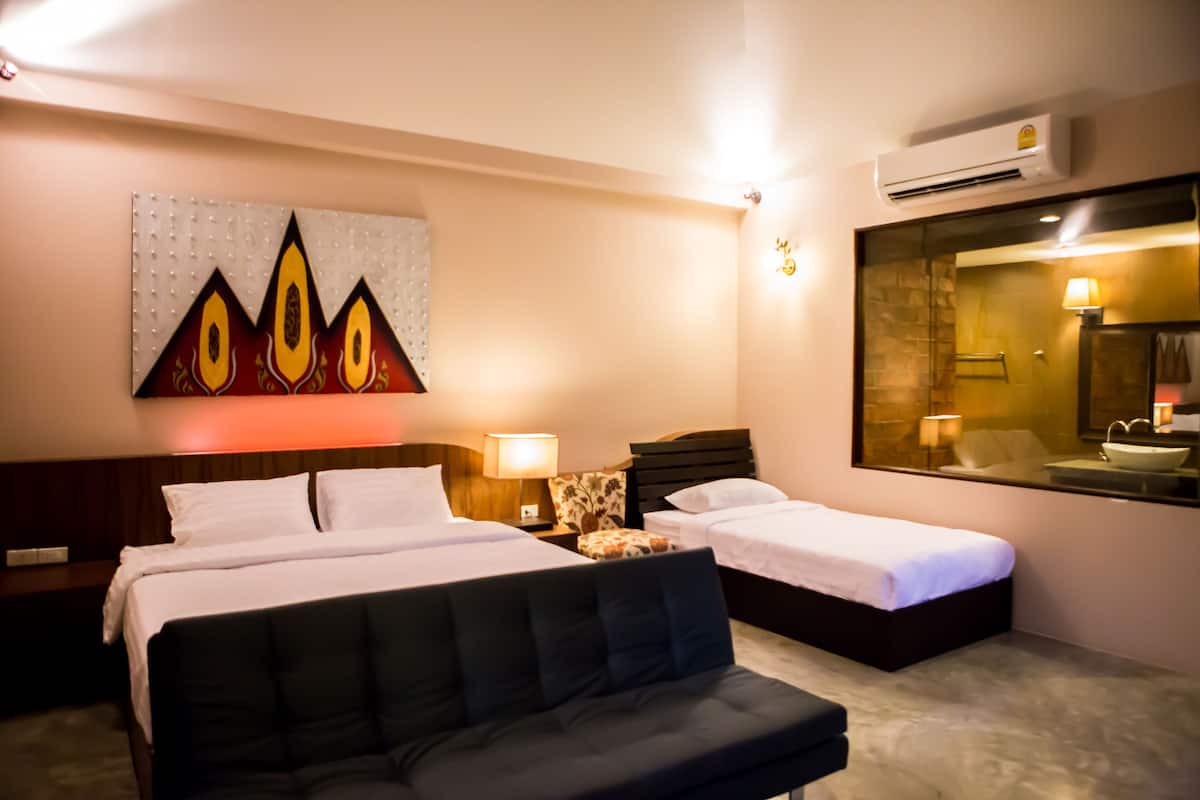 A hotel room with a large bed, two smaller beds, a sofa, a painting, a mirror, and a bathroom with a sink and mirror.