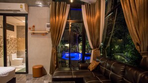 A modern hotel room with a leather sofa, a glass coffee table, and a view of a swimming pool at night.