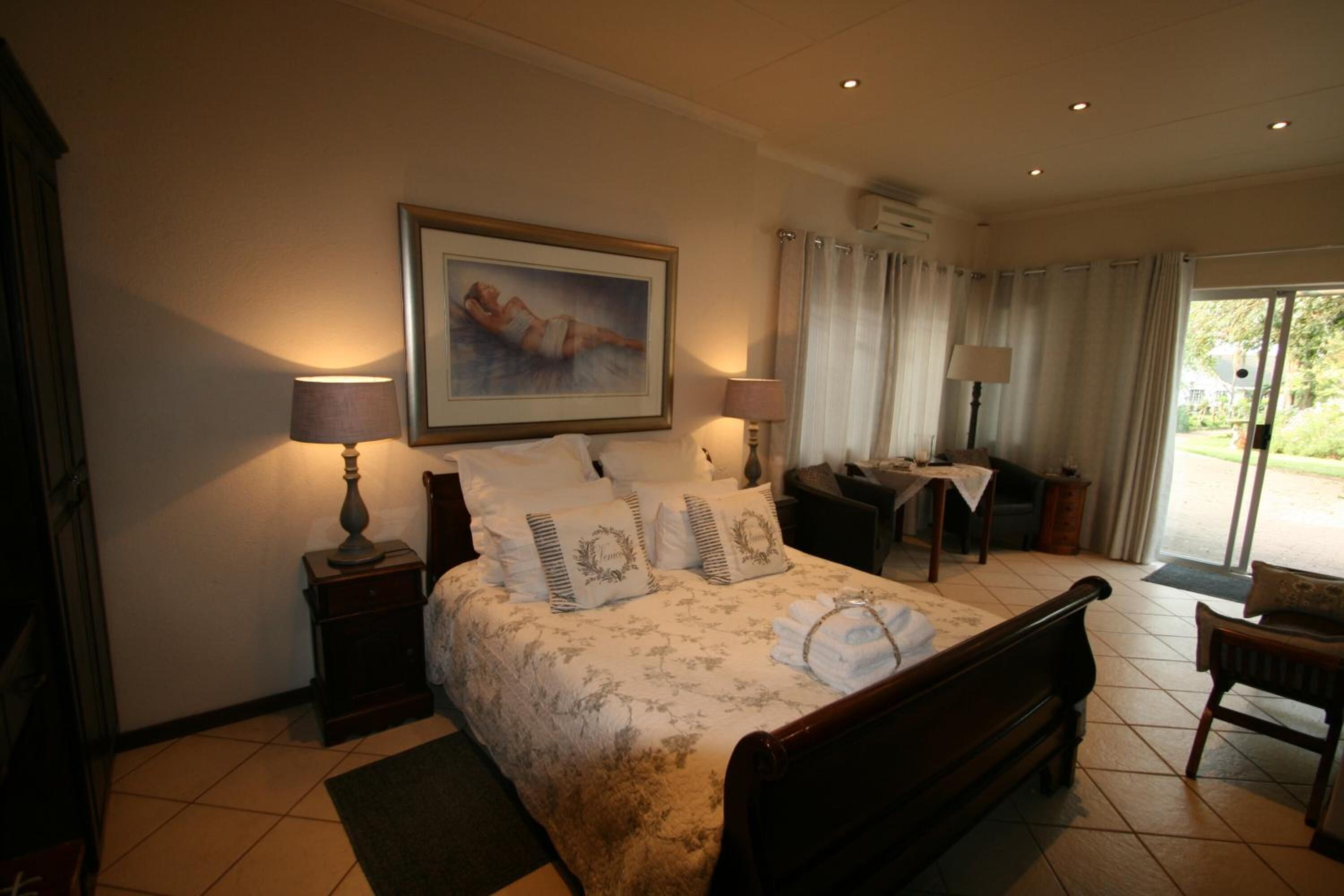 Une chambre à coucher comprenant un lit, deux tables de chevet avec des lampes, une chaise, un bureau et une fenêtre avec des rideaux.