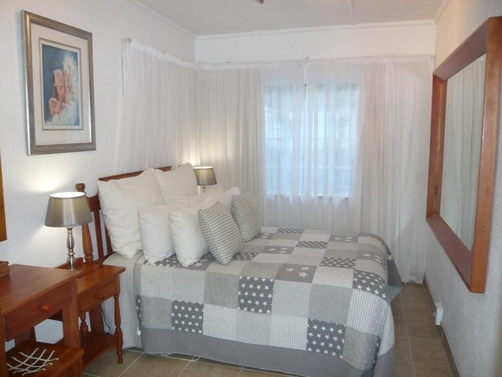 A bedroom with a bed, two bedside tables, a lamp, a framed picture on the wall, and a window with curtains.