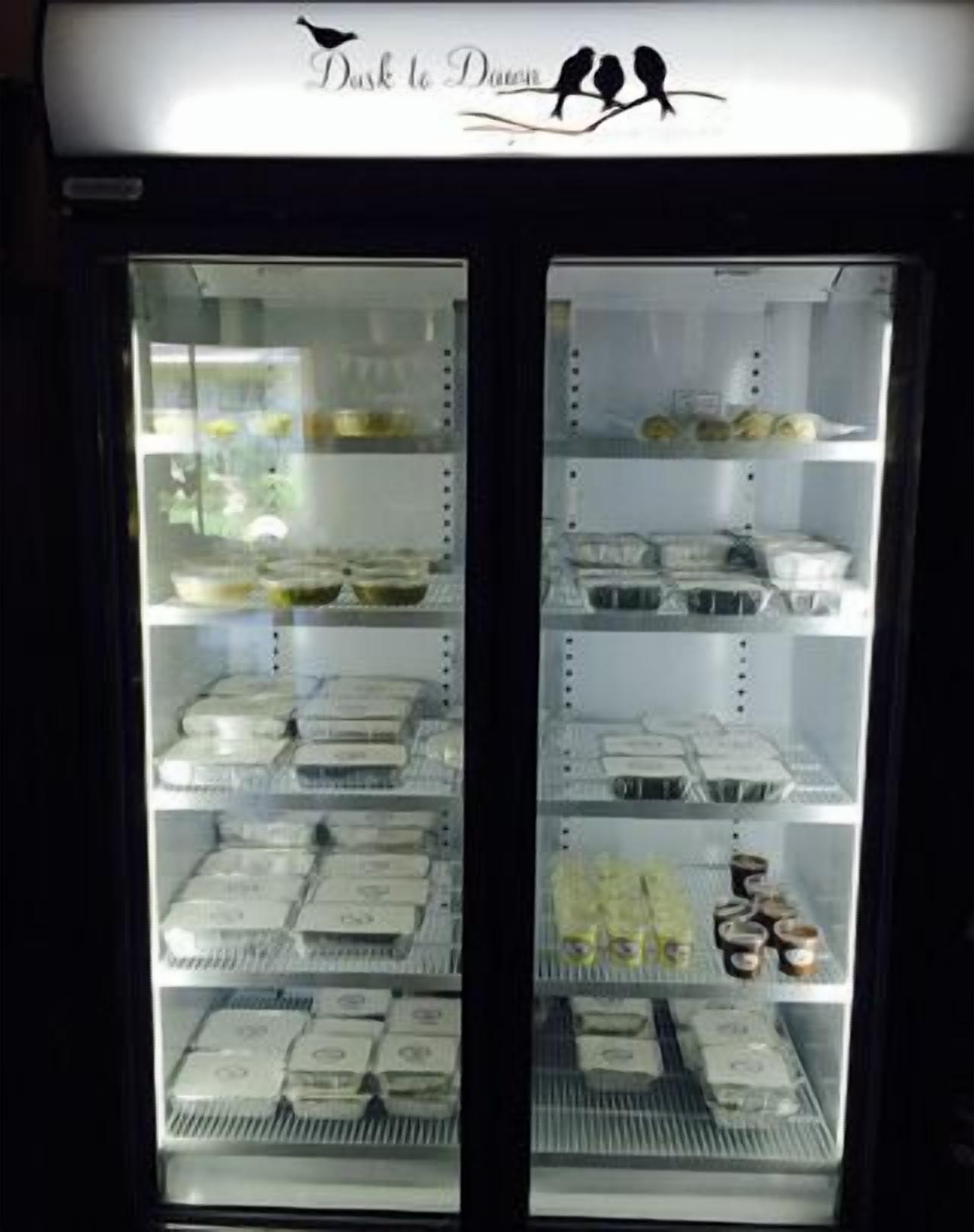 Vitrina refrigerada con diferentes productos alimenticios, como bandejas de pasteles y tazones de sopa.