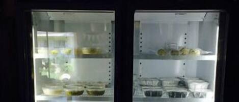 Vitrina refrigerada con diferentes productos alimenticios, como bandejas de pasteles y tazones de sopa.
