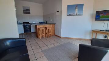A compact living space with a kitchenette, a TV mounted on the wall, and a small seating area with two chairs.