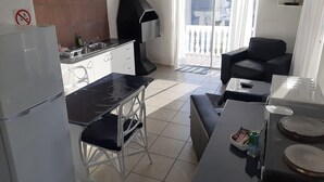 Cocina compacta con estufa, lavamanos y una campana grande negra.  Comedor con mesa y sillas, y un sofá negro. Un televisor está montado en la pared sobre el sofá.