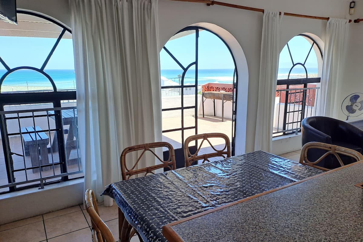Ein Essbereich mit Tisch und Stühlen, große Bogenfenster mit Meerblick und ein Balkon mit Sitzgelegenheit im Freien.