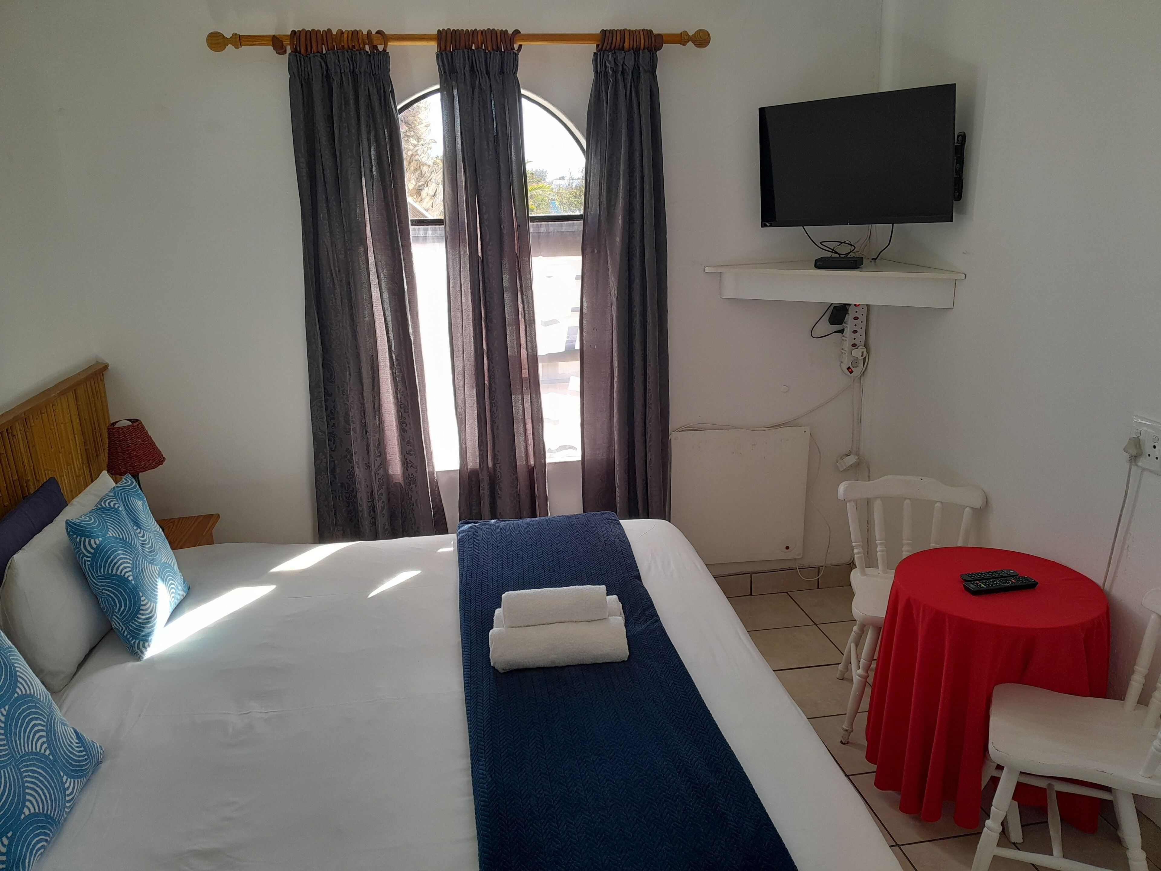 A hotel room with a bed, a TV, a small table with a chair, and a window with curtains.