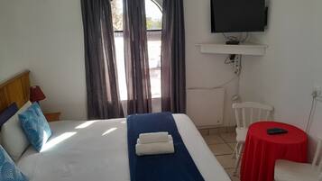 A hotel room with a bed, a TV, a small table with a chair, and a window with curtains.