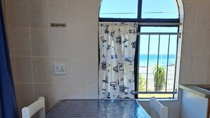 Un comedor con una mesa cubierta por un mantel azul, sillas blancas, una ventana con vista al mar y un cartel de 'NO FUMAR' en la pared.