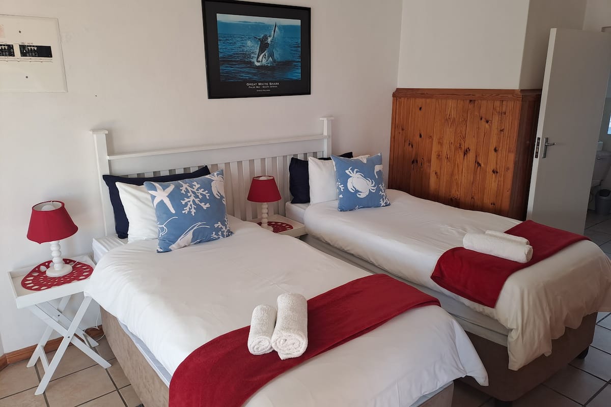 Ein Hotelzimmer mit zwei Betten, jeweils mit weißer Bettwäsche und roten Akzenten, einem Holzschrank und einem gerahmten Bild an der Wand.