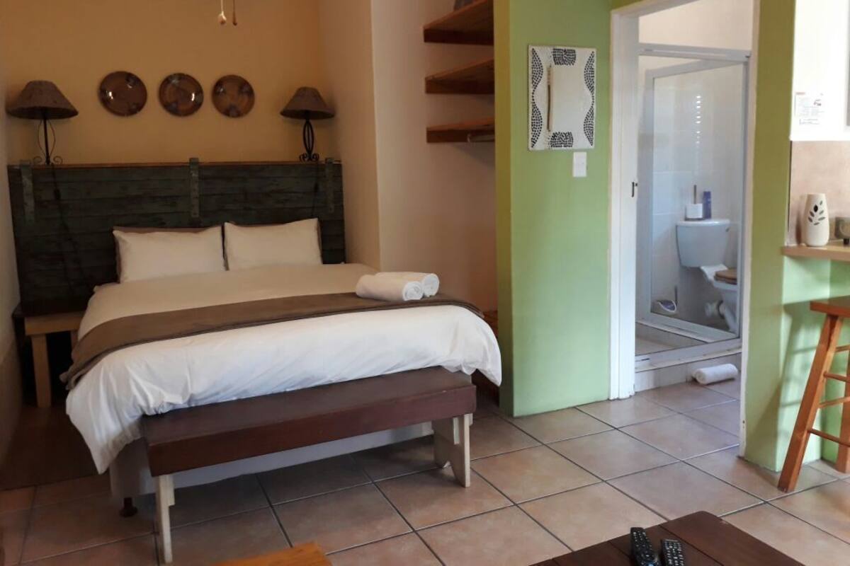 Une chambre à coucher avec un lit, des lampes de chevet, un banc, une porte de salle de bain et une petite table avec une télécommande.