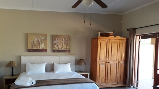 A bedroom with a bed, two nightstands, a wooden wardrobe, a ceiling fan, and a door leading outside. - Tourist Lodge Gansbaai (Gansbaai)