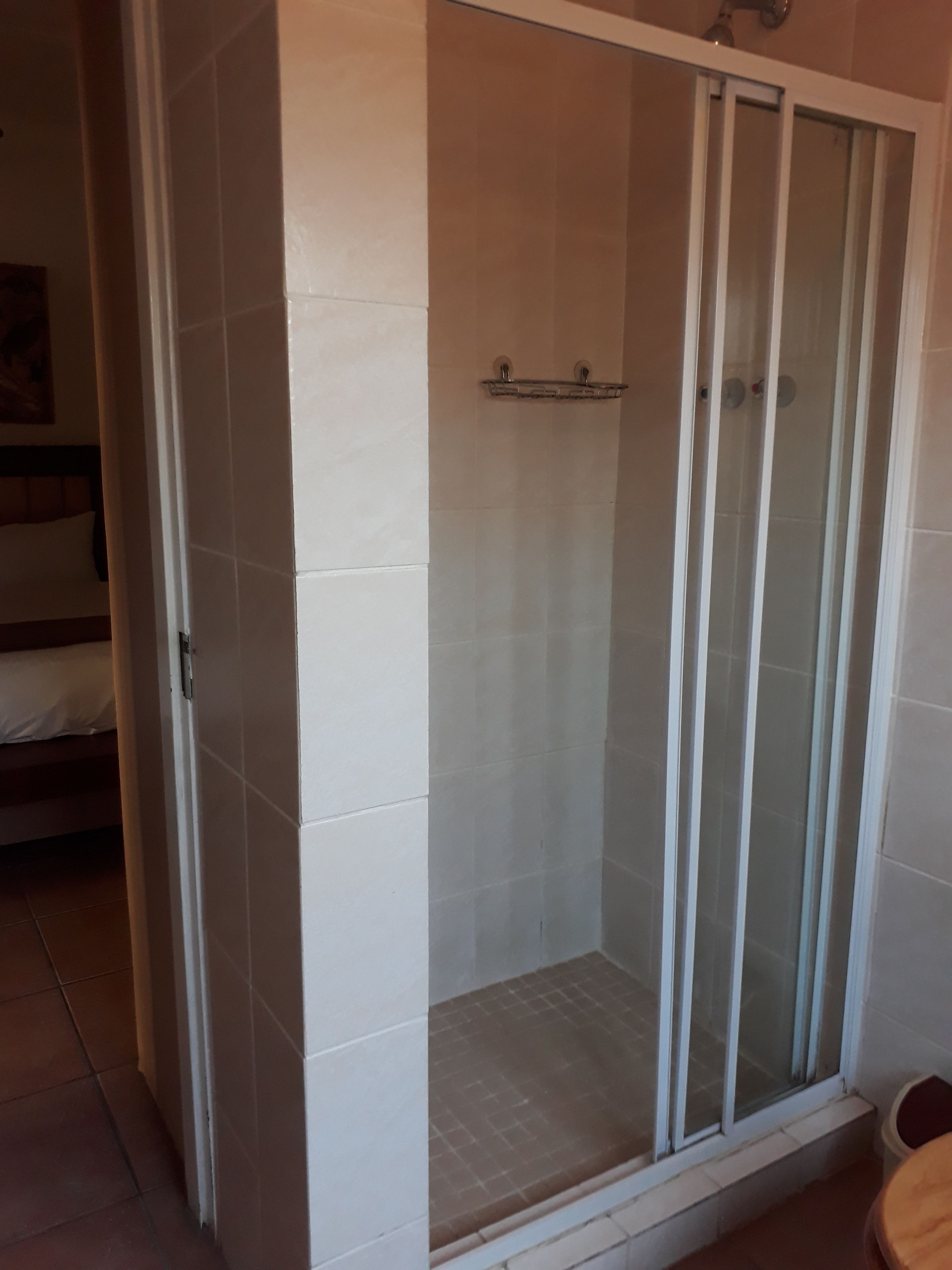 A shower area with a glass door, white tiled walls, and a small shelf.