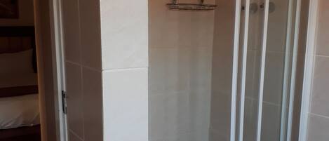 A shower area with a glass door, white tiled walls, and a small shelf.