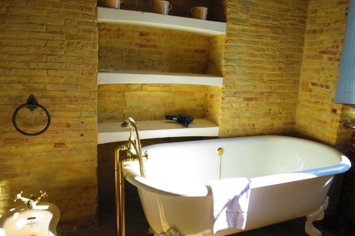 Un baño con una bañera tipo pata de león blanca, un lavamanos blanco y un estante con tazas.