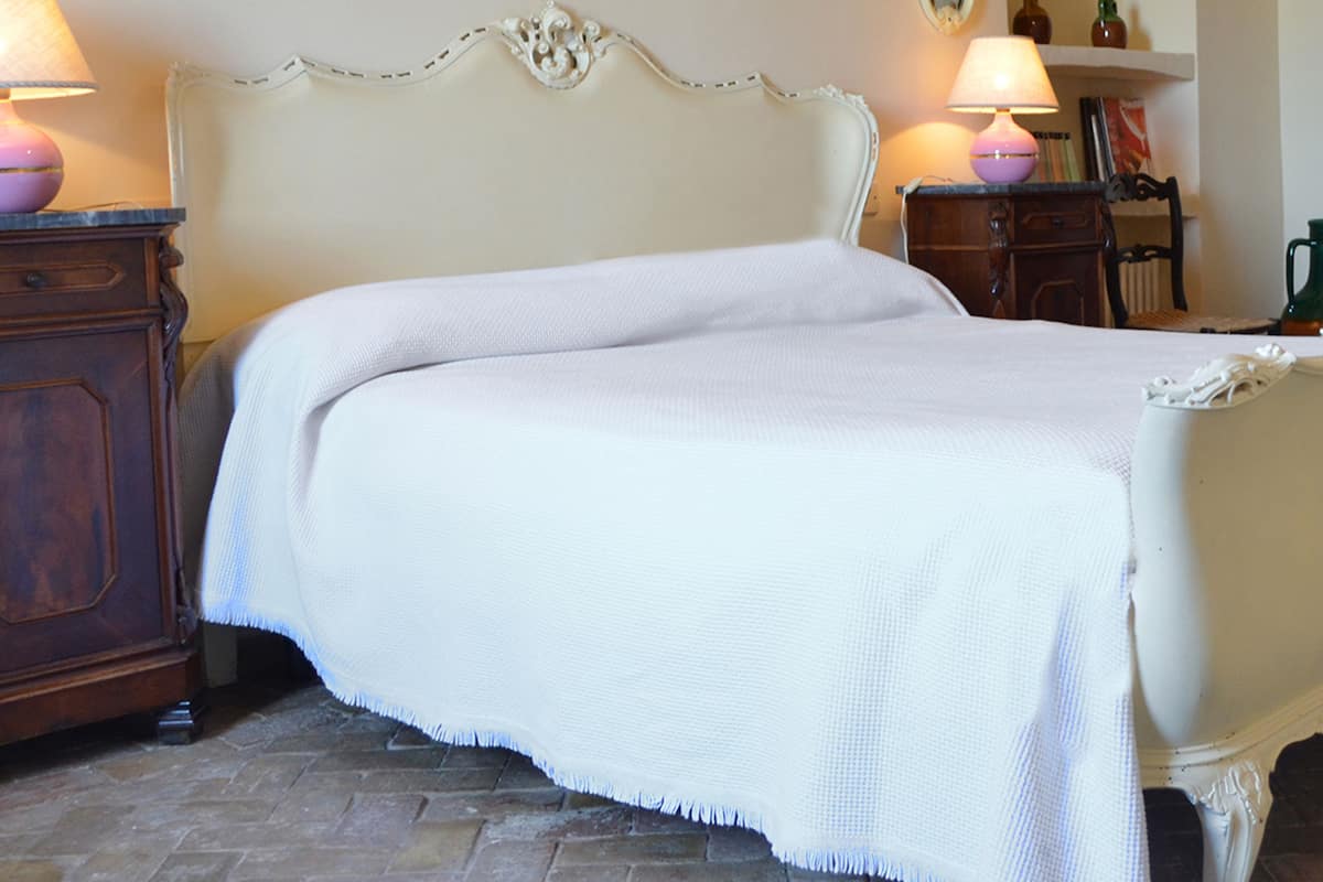 Ein Bett mit weißem Kopfteil und weißer Bettdecke in einem Zimmer mit Ziegelboden.