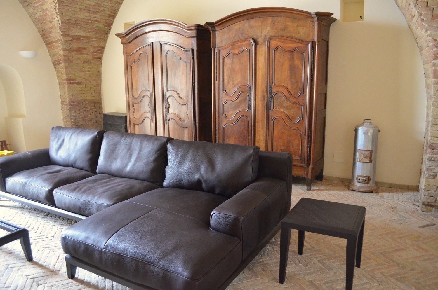 A living room with a dark leather sofa, a matching ottoman, and a wooden cabinet with decorative carvings.