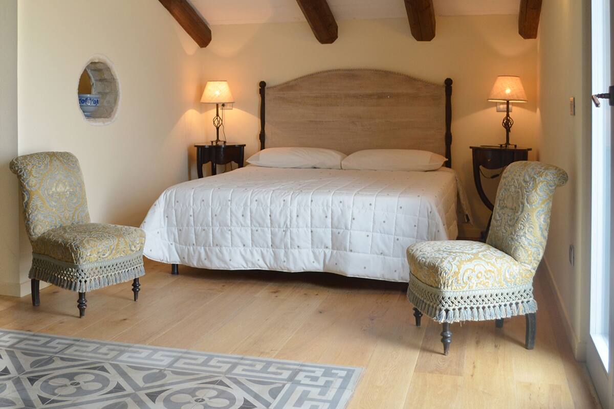 Ein Schlafzimmer mit Holzboden, einem großen Bett, zwei Stühlen und zwei Nachttischlampen.