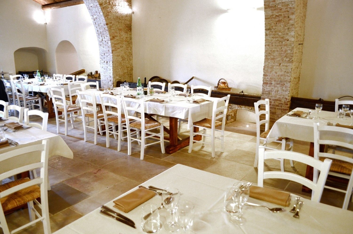Un restaurante con mesas y sillas blancas, dispuestas en un amplio comedor con paredes de ladrillo y techos abovedados.