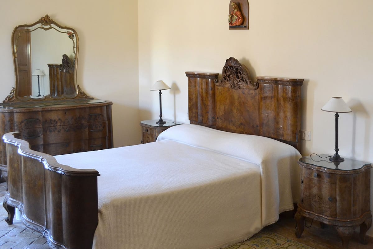 Ein Schlafzimmer mit einem großen Bett, zwei Nachttischen, einer Kommode, einem Spiegel und einer Wanddekoration.