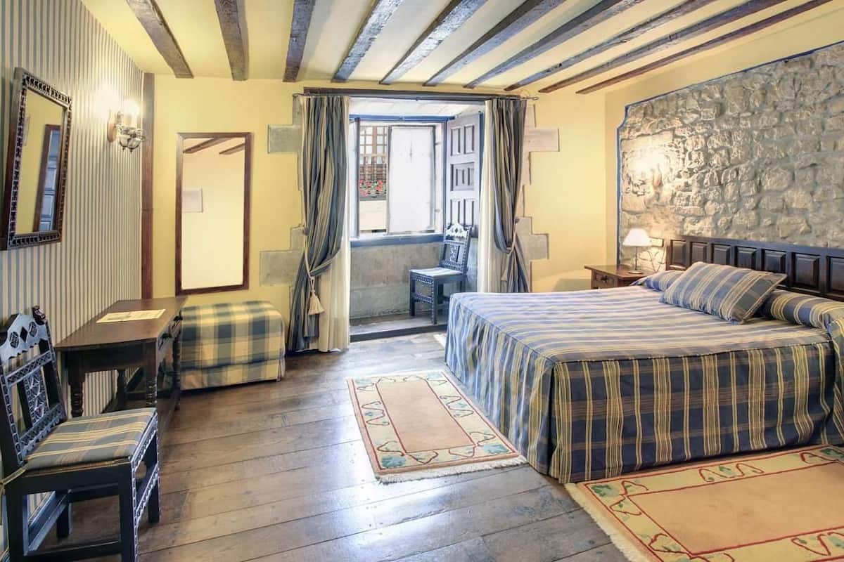 Une chambre confortable avec un lit, une chaise en bois, une petite table et un mur en pierre.