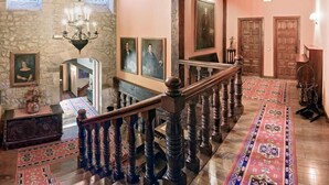 Una imponente escalera con barandales ornamentados, un muro de piedra y una gran puerta de madera.