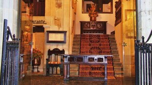 Una entrada imponente con una escalera que conduce a un nivel superior, con un candelabro, cuadros enmarcados y un cartel sobre la puerta.