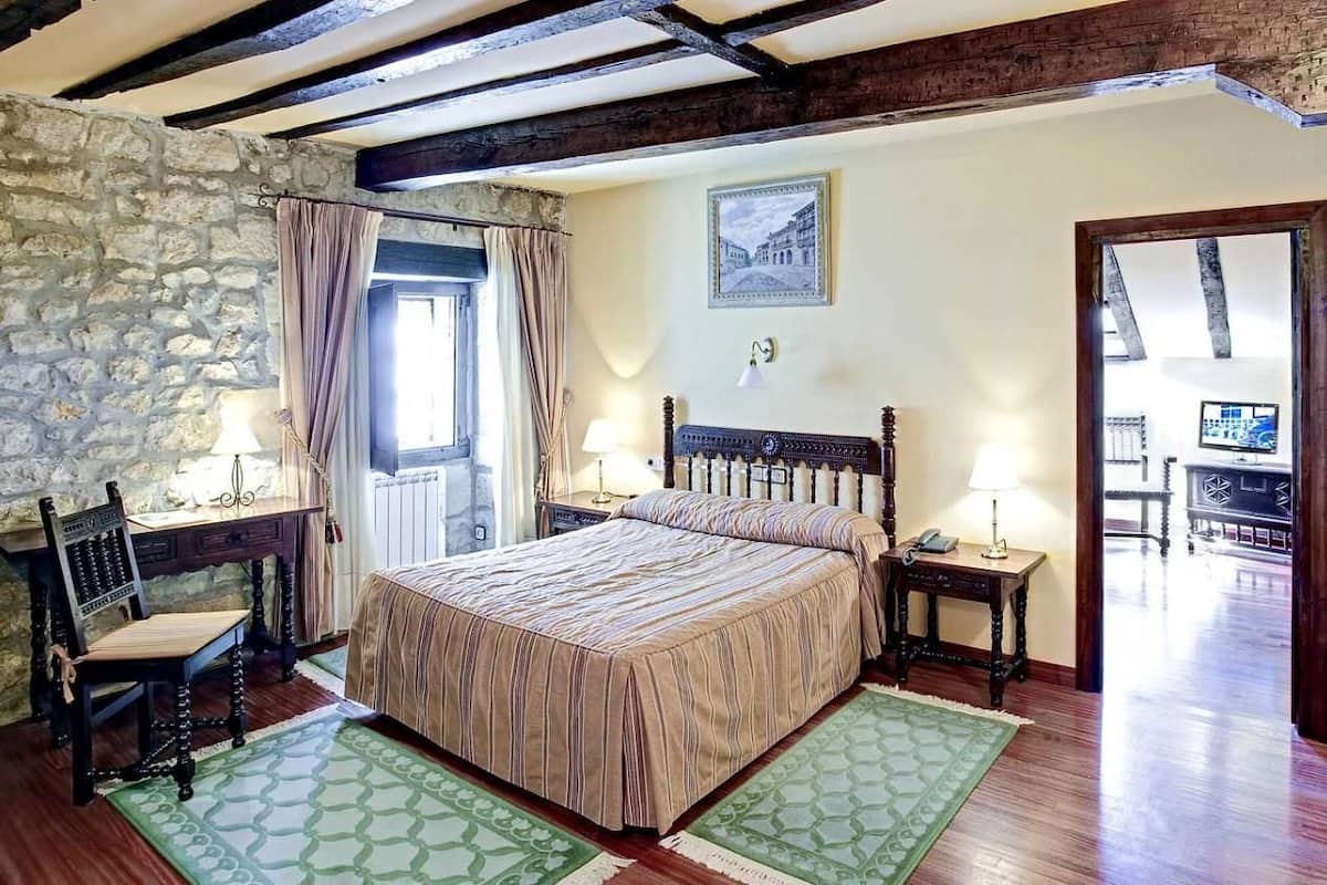Une chambre avec un grand lit, un mur en pierre, un bureau en bois et une vue sur l’extérieur.