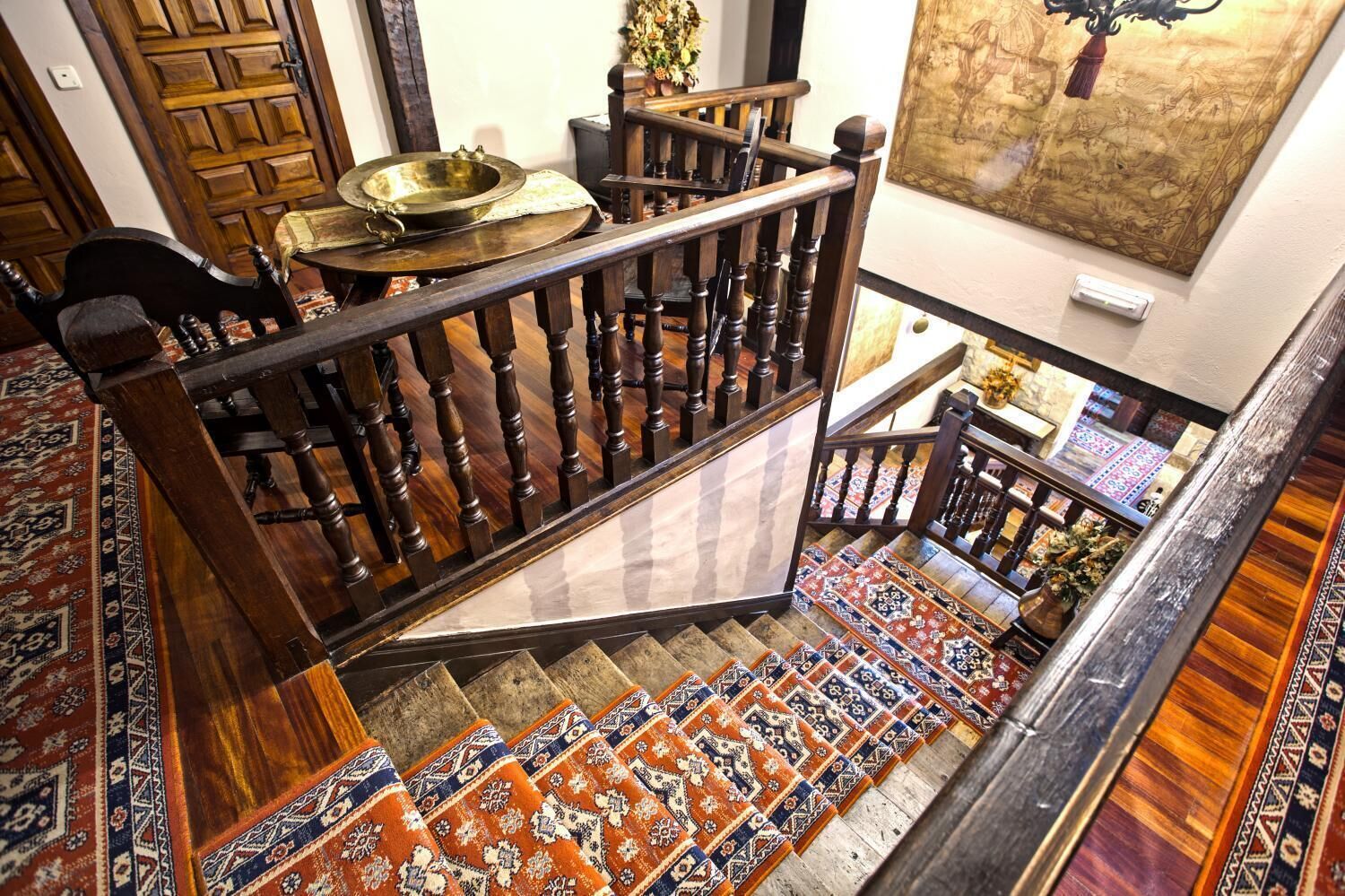 A wooden staircase with a patterned carpet, a brass bowl, and a framed artwork on the wall.