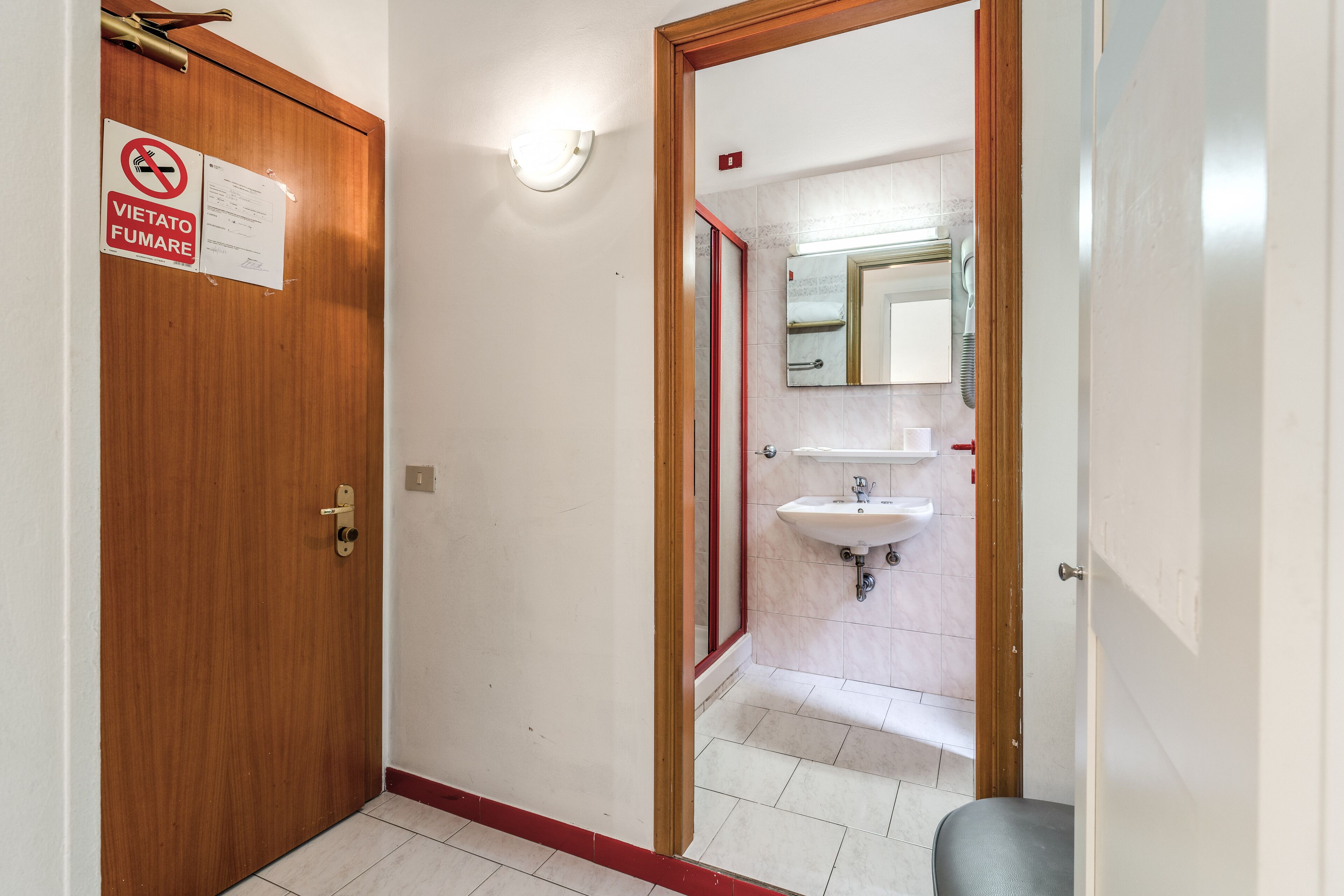 A hallway with a wooden door, a no smoking sign, a mirror, and a sink.