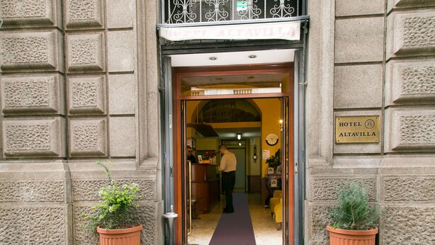 L’entrée d’un hôtel, avec un comptoir d’accueil, une horloge et une enseigne indiquant le nom de l’hôtel.