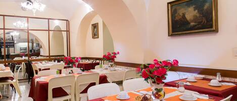 A dining area with tables set for breakfast, featuring orange placemats and white tablecloths.