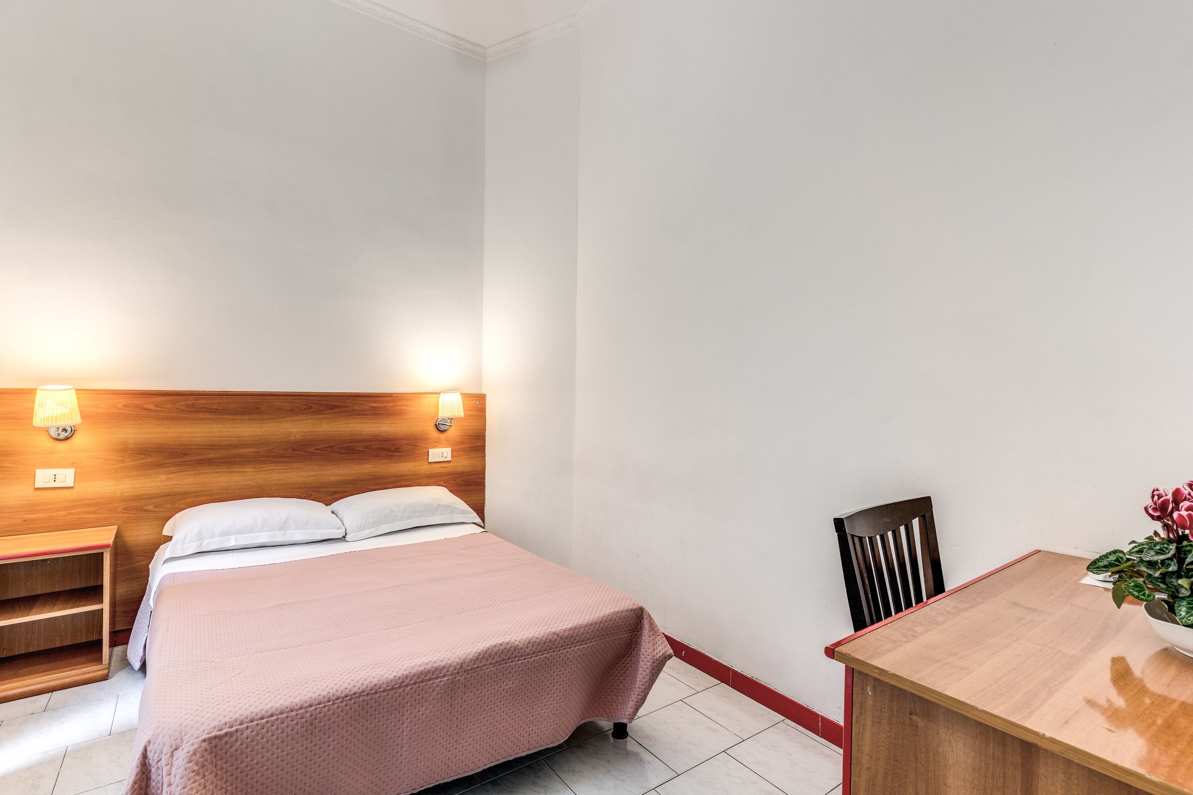 Quarto de hotel com cama, mesas de cabeceira, escrivaninha e cadeira.