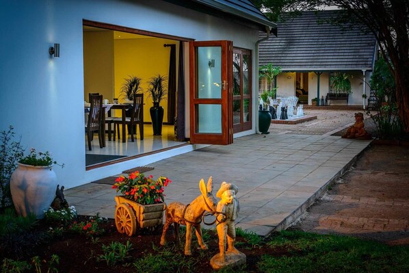 A modern building with a glass door entrance, a patio with outdoor furniture, and a garden with a statue of a horse and rider.