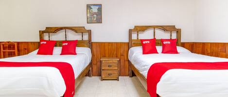 A hotel room with two wooden beds, each with white bedding and red pillows, and a small wooden nightstand between them.