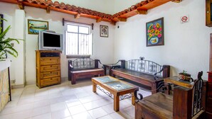 Una sala de estar con un banco de madera, un televisor sobre un mueble de madera, una ventana y un cuadro en la pared.